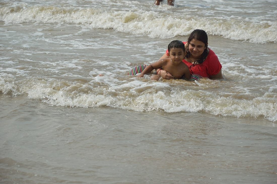 Mujer sujeta a un niño pequeño entre las olas en la orilla, situación de riesgo de ahogamiento secundario