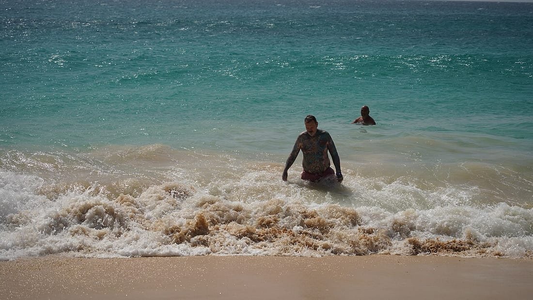 Hombre saliendo del mar entre las olas en una playa, escena ligada al mito del corte de digestión