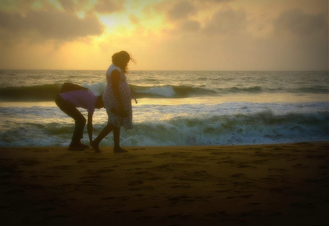 Mujer embarazada en la playa caminando por la orilla al atardecer junto a su pareja