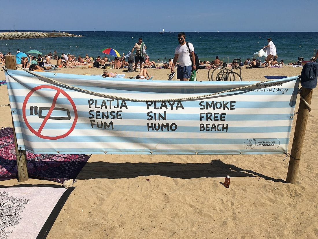 Pancarta "Playa sin humo" del Ayuntamiento de Barcelona en la arena, recordando la prohibición de fumar en la playa