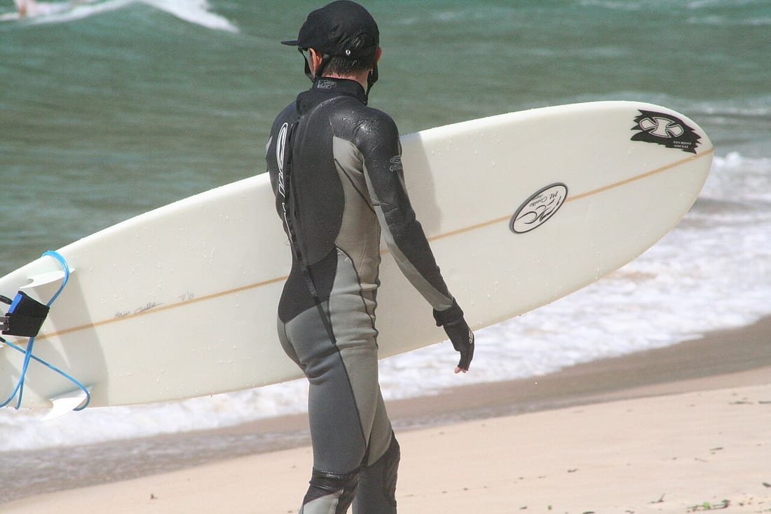 Surfista con traje de neopreno integral caminando por la orilla con la tabla bajo el brazo