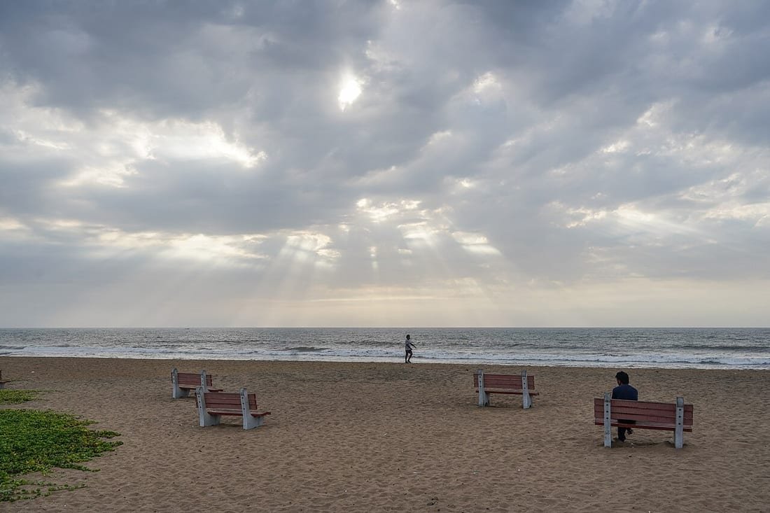 Playa con bancos, mar y cielo nuboso con rayos de sol, ilustrando la predicción de playas AEMET