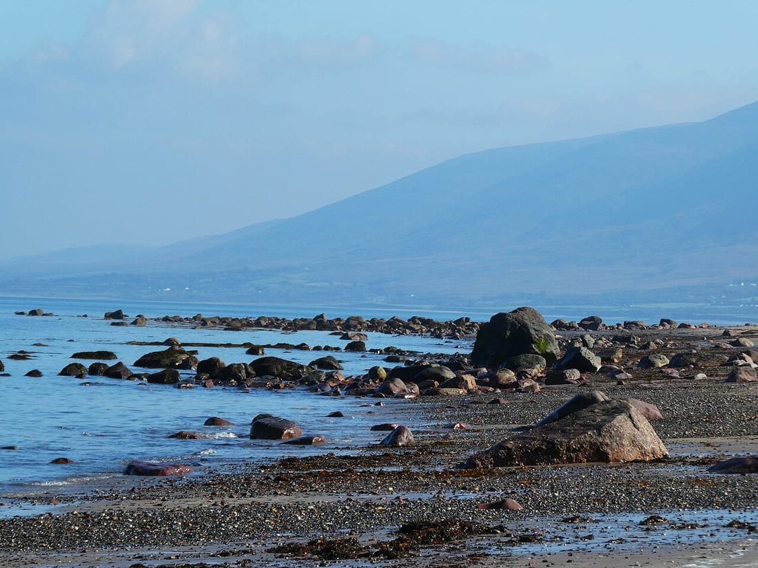 Playa rocosa con marea baja y montaña al fondo, útil para saber cómo leer las tablas de mareas