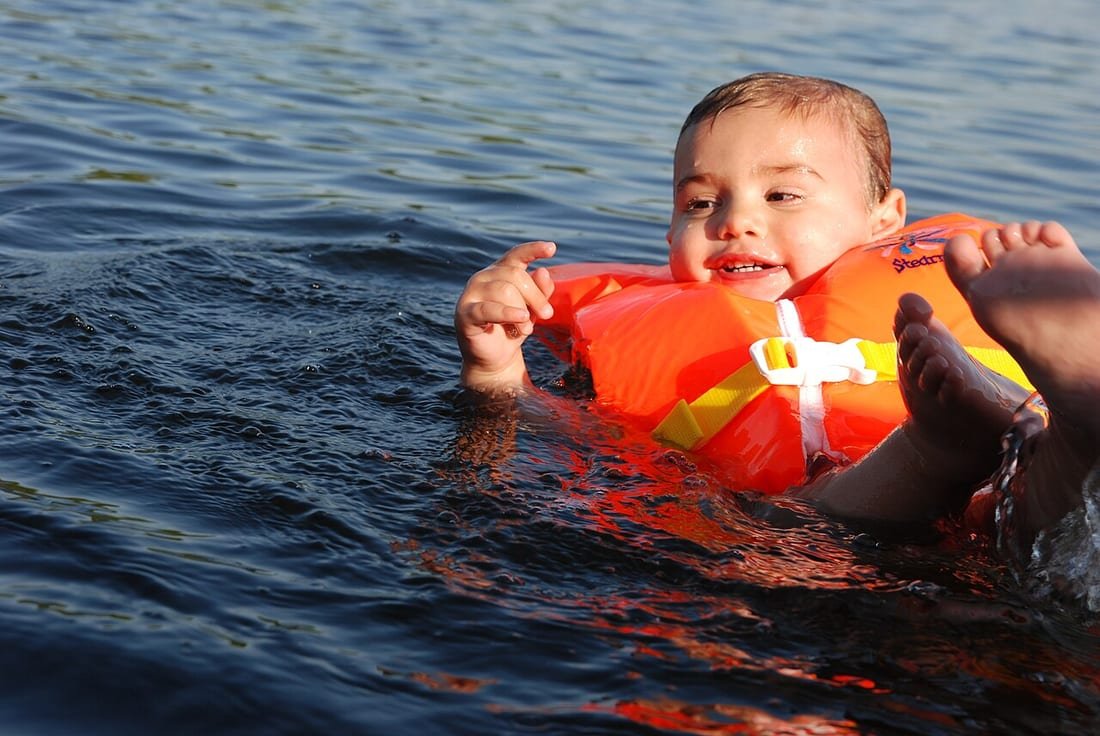 Niño pequeño en el agua con chaleco salvavidas naranja: manguitos o chaleco salvavidas niños