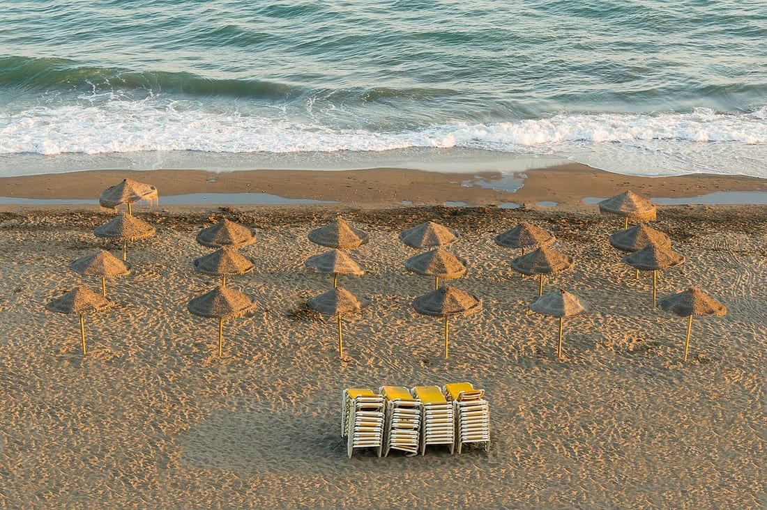 Hileras de sombrillas de paja clavadas en la arena de la playa junto al mar, tema clavar sombrilla playa viento