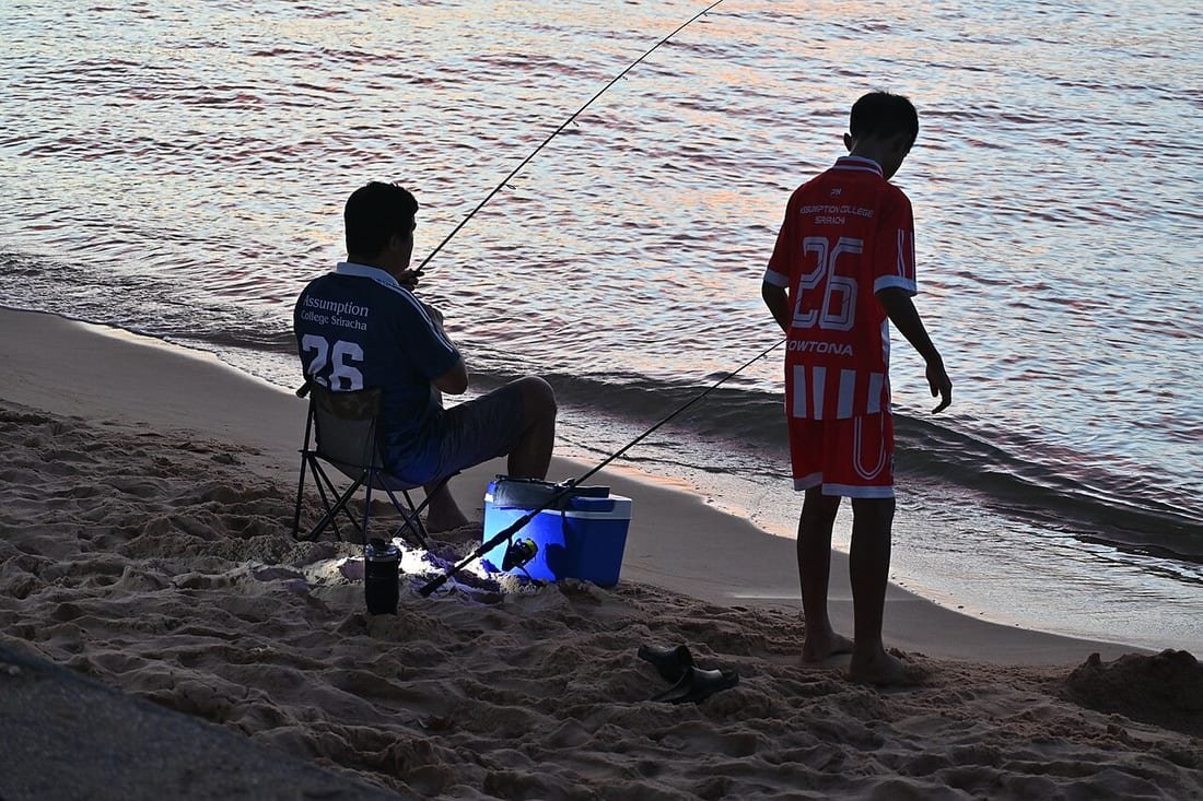 Nevera de playa azul para conservar comida junto a dos pescadores en la arena al atardecer