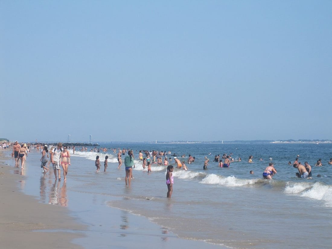 Playa concurrida con bañistas y niños en la orilla, escena donde un niño perdido en la playa es un riesgo