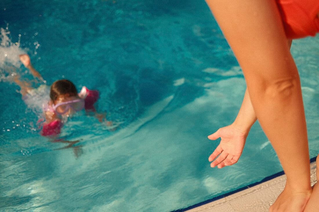 Niño nadando en el agua mientras un adulto lo vigila, contexto de la otitis del nadador