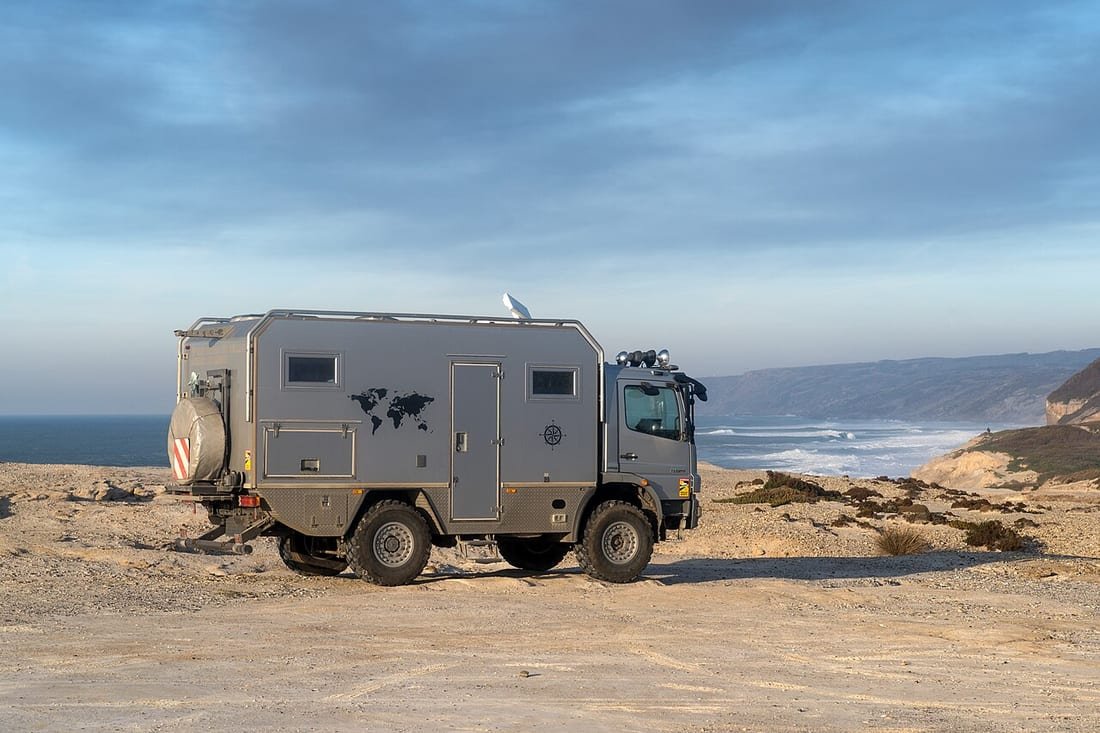 Autocaravana camper gris aparcada sobre arena junto al mar, ideal para pernoctar en autocaravana en la playa