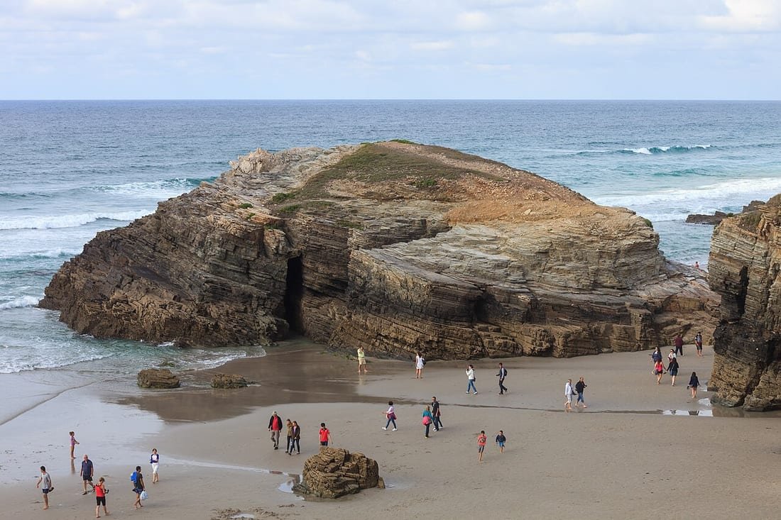Bañistas paseando entre los arcos de roca de la playa de As Catedrais, en Ribadeo, con la marea baja