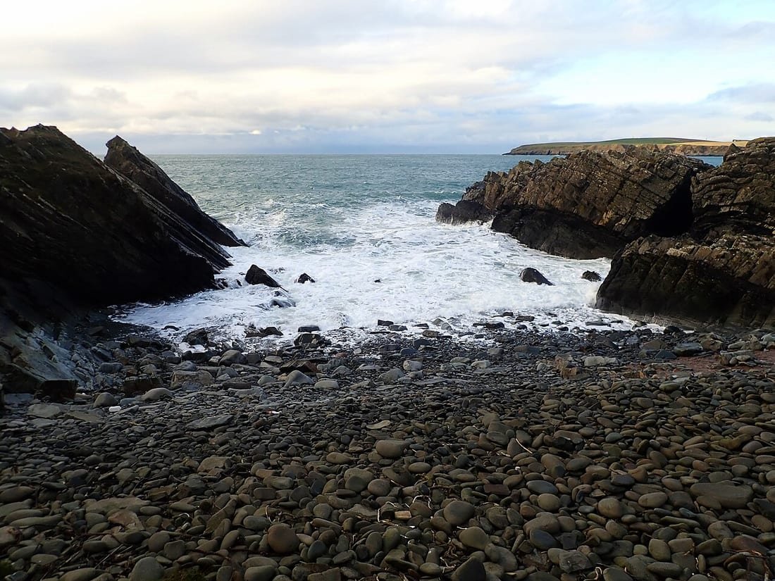 Playa de cantos rodados en pendiente, con las olas rompiendo directamente sobre la orilla