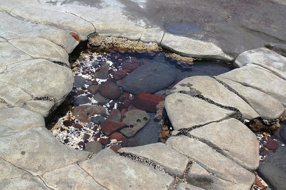Poza de marea entre rocas con agua clara y guijarros, ejemplo de pozas de marea piscinas naturales