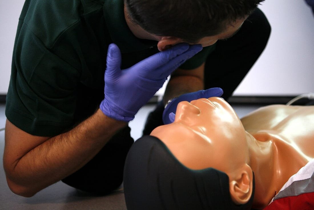 Socorrista con guantes practica ventilación de rescate en maniquí de RCP, primeros auxilios ahogamiento