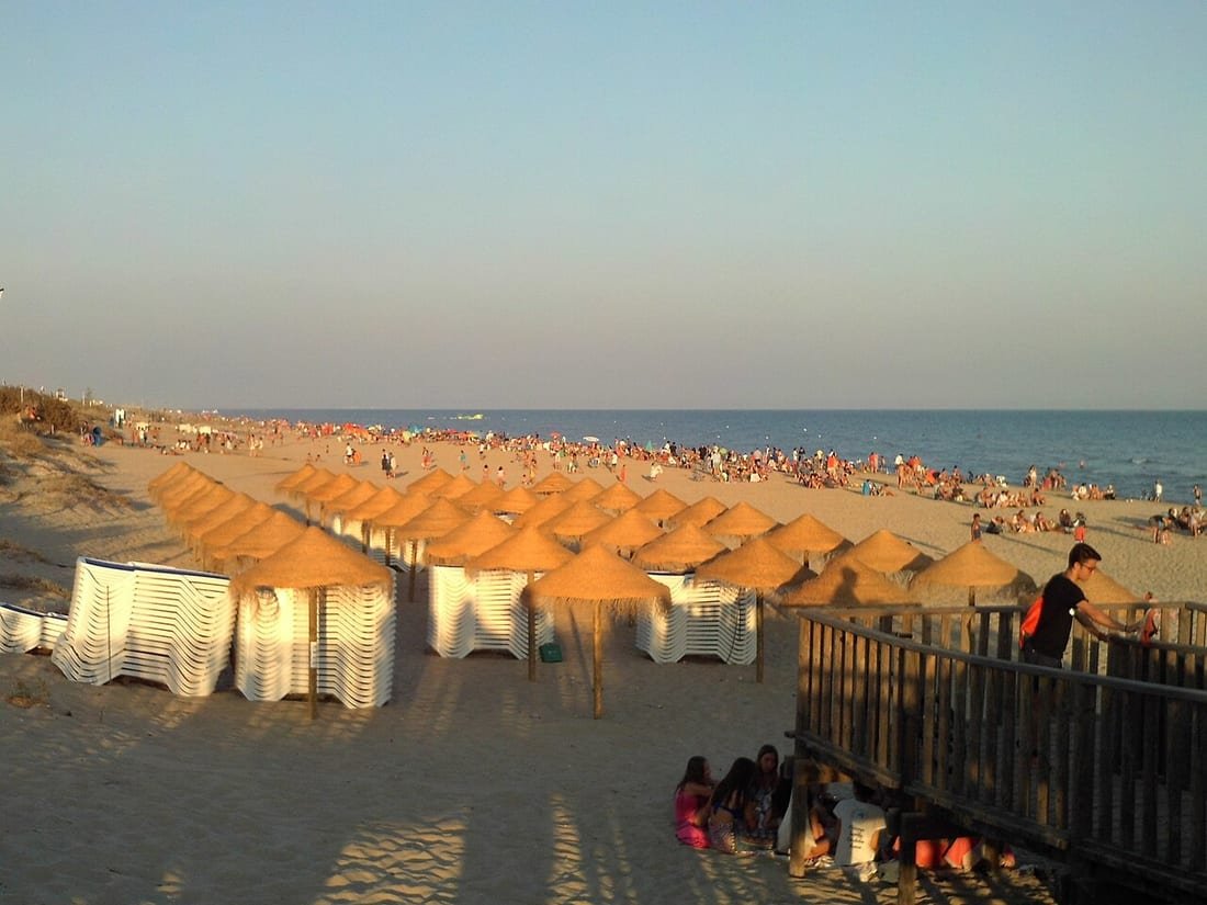 Sombrillas de paja y hamacas alineadas en la arena de una playa española al atardecer