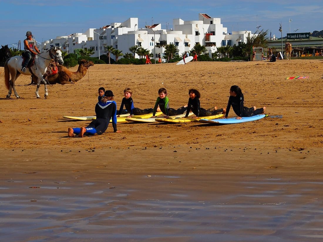 Niños con neopreno tumbados sobre tablas en la arena en una clase de surf para principiantes